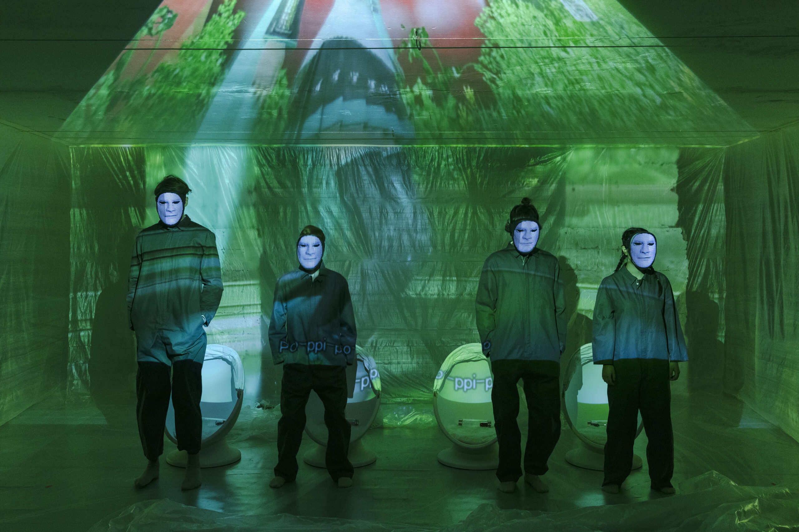 Štyria ľudia v zelenom svetle s projekciou na tvárach stojí v miestnosti.